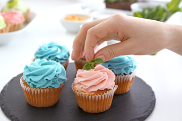 Young female confectioner decorating cupcakes in kitchen, closeup