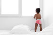 © Lisa Tichané - Black baby boy standing on bed looking out by the window