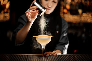 Professional bartender girl holding a spice shaker adding to a delicious cocktail flavours