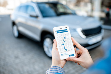 Woman using smart phone with navigation app, close-up view with modern car on the background