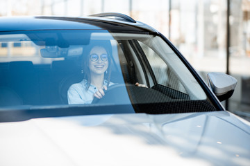 Wall Mural - Young and happy woman driving a luxury car in the city, front view through the windshield