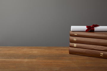 Wall Mural - Brown books and diploma with red ribbon on wooden surface on grey