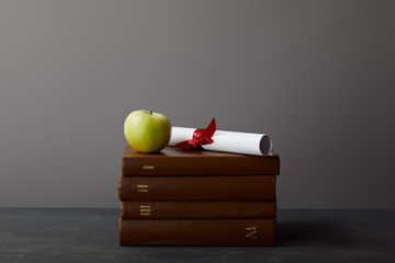 Poster - Brown books, diploma with ribbon and green apple on textured surface on grey