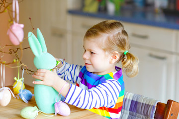 Cute little toddler girl decorating tree and bunny with colored pastel plastic eggs. Happy baby child having fun with Easter decorations. Adorable healthy smiling kid in enjoying family holiday