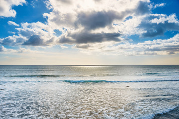 seascape with silver sunlight reflection, calm waves, bright sky and white clouds