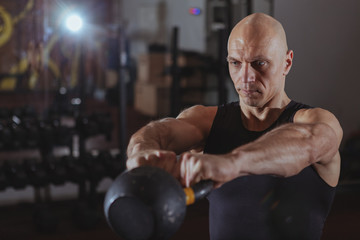 Mature athletic man working out with kettlebell at crossfit box gym. Concentrated muscular sportsman doing kettlebell swings, copy space. Crossfit, strength concept