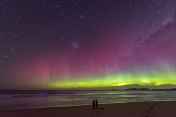 two people in silhouette standing in awe of an incredible display of the aurora australis or souther
