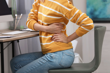 Wall Mural - Young woman suffering from back pain in office, closeup