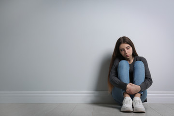 Wall Mural - Upset teenage girl sitting on floor near wall. Space for text