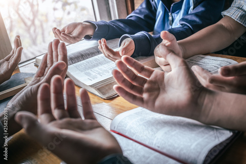 Cuadros en Lienzo Christian children group praying together around wooden table with open bible page at home, prayer meeting concept