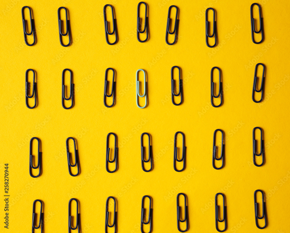 White paper clip among black ones on color background. Concept of uniqueness