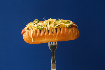 Fork with tasty hot dog on color background