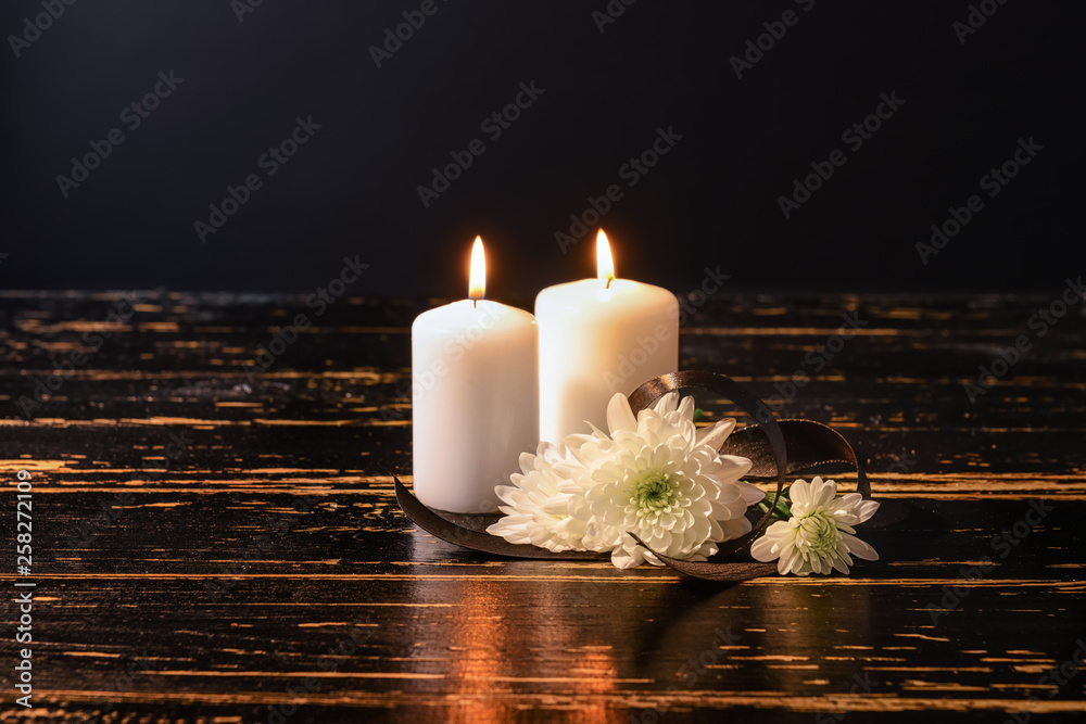 Burning candles and flowers on table against black background