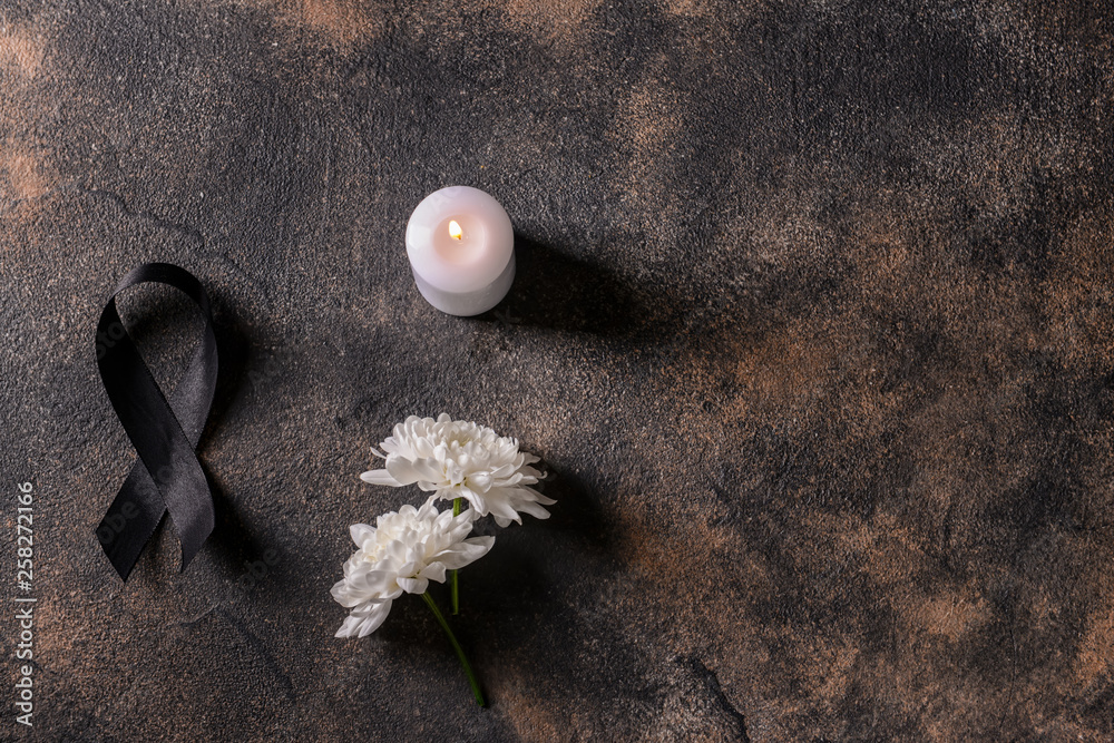 Black mourning ribbon, flowers and candle on grunge background