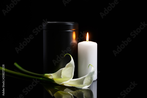 Fotografía Mortuary urn, burning candle and flowers on dark background