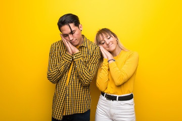 Wall Mural - Young couple over vibrant yellow background making sleep gesture in dorable expression