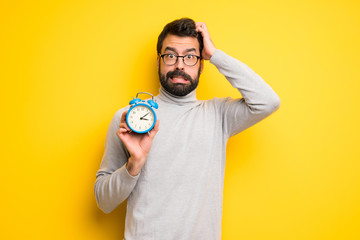 Wall Mural - Man with beard and turtleneck restless because it has become late and holding vintage alarm clock
