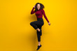 © luismolinero - Dominican woman with curly hair jumping over isolated yellow wall