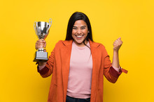 Young Colombian Girl Over Yellow Wall Holding A Trophy