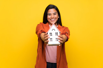 Wall Mural - Young Colombian girl over yellow wall holding a little house