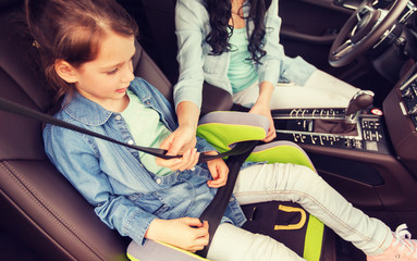 Poster - family, transport, road trip and people concept - happy woman fastening child with safety seat belt in car