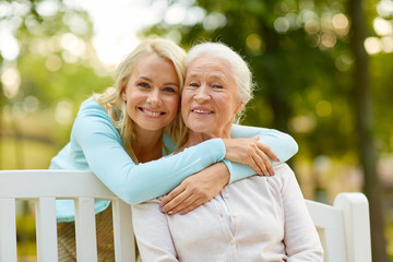 family, generation and people concept - happy smiling young daughter with senior mother sitting on p