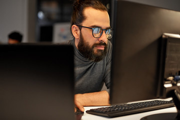 deadline, technology and people concept - close up of creative man in glasses working at night office and thinking