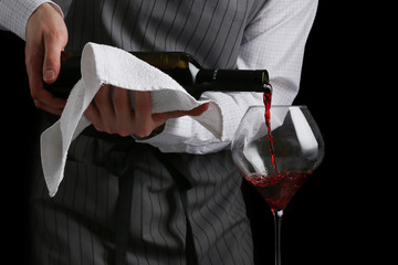 Wall Mural - the waiter pours wine in glass on dark background