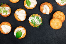 A Photo Of Salt Crackers With Soft Cream Cheese Spread And Herbs, Shot From The Top On A Black Background With A Place For Text