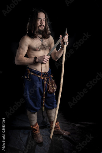 A Strong Bearded Long Haired Man With A Tattoo On His Shoulder Is