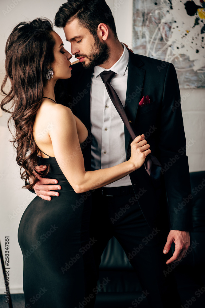attractive woman in black dress holding tie of passionate man standing in suit Stock Photo | Adobe Stock attractive woman in black dress holding tie of passionate man standing in suit Stock Photo | Adobe Stock