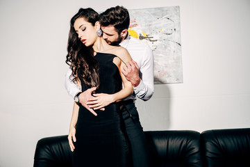 bearded man kissing and touching brunette woman in black dress