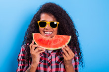 Pretty Young Girl Holding Slice Of Watermelon In Front Of Her Face. Portrait Of Smiling African American Girl Isolated On Blue Background. Healthy & Happy - Imagem