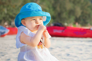 Greedy girl eats something on the beach and does not want to share. She is in white dress and blue hat