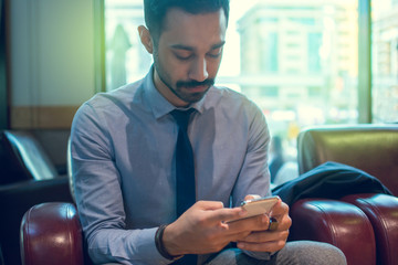 Close up portrait of young business man using mobile phone while sitting in comfortable chair indoors