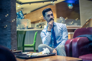 Wall Mural - Portrait of handsome young businessman with hand on chin and pensive expression relaxing after having a meal in cafe during office break.