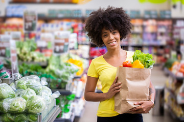 Healthy positive happy african woman holding a paper shopping bag full of fruit and vegetables