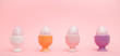 Row of speckled eggs in egg cups on pink