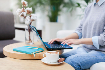 Freelancer is working in comfortable cafe. Girl is using laptop in coworking modern office. Businesswoman is enjoying coffee. Wellbeing in workplace. Close up of hands.