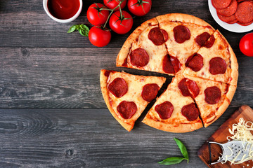 Wall Mural - Traditional pepperoni pizza with cut slices. Top view corner border against a wood background with copy space.