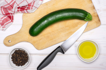 Wall Mural - One whole zucchini is ready to be chopped. recipe step by step fusilli pasta with zucchini on chopping board with a knife and a tea towel flatlay on white wood