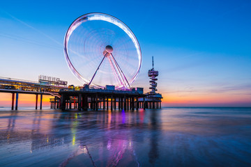 Colorful blue hour sunset on coastline, beach, pier and ferris wheel, Scheveningen, the Hague.