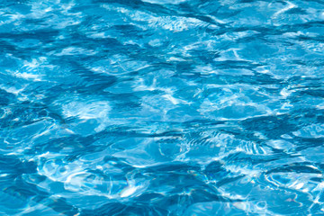 blue and bright ripple water surface in swimming pool with sun reflection.