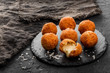Fried potato cheese balls or croquettes with spices on black plate over dark stone background. Unhealthy food
