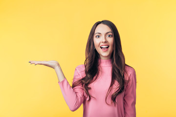Wall Mural - Beautiful smiling woman holding and presenting copy space on her palm isolated on yellow background