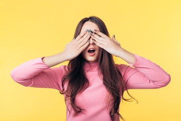 Wall Mural - Surprised excited woman closed her eyes with hands waiting for surprise isolated on yellow background