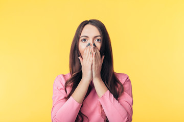 Wall Mural - Shocked excited woman covering her mouth with hands on yellow background