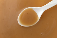 Top View Of Creamy Brown Turkey Gravy With A White Spoon In The Food.