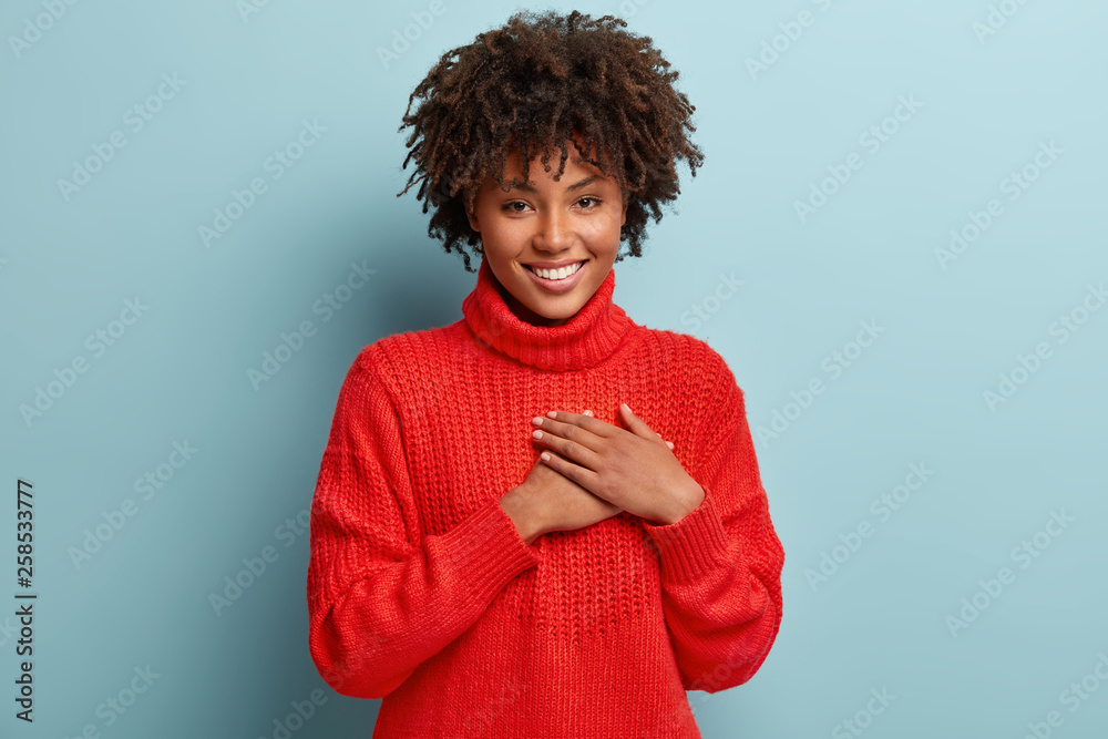 Photo of emotional dark skinned female touches heart with both palms, demonstrates thankful gesture, has good natured expression, expresses great sympathy, gratitude with honesty, feels love - obrazy, fototapety, plakaty 