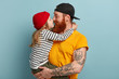 © WHstudio Leushin N - Sideways shot of affectionate dad holds small child who embraces and kisses father, demonstrate friendly relationships, mutual love, isolated over blue background. Fatherhood and children concept